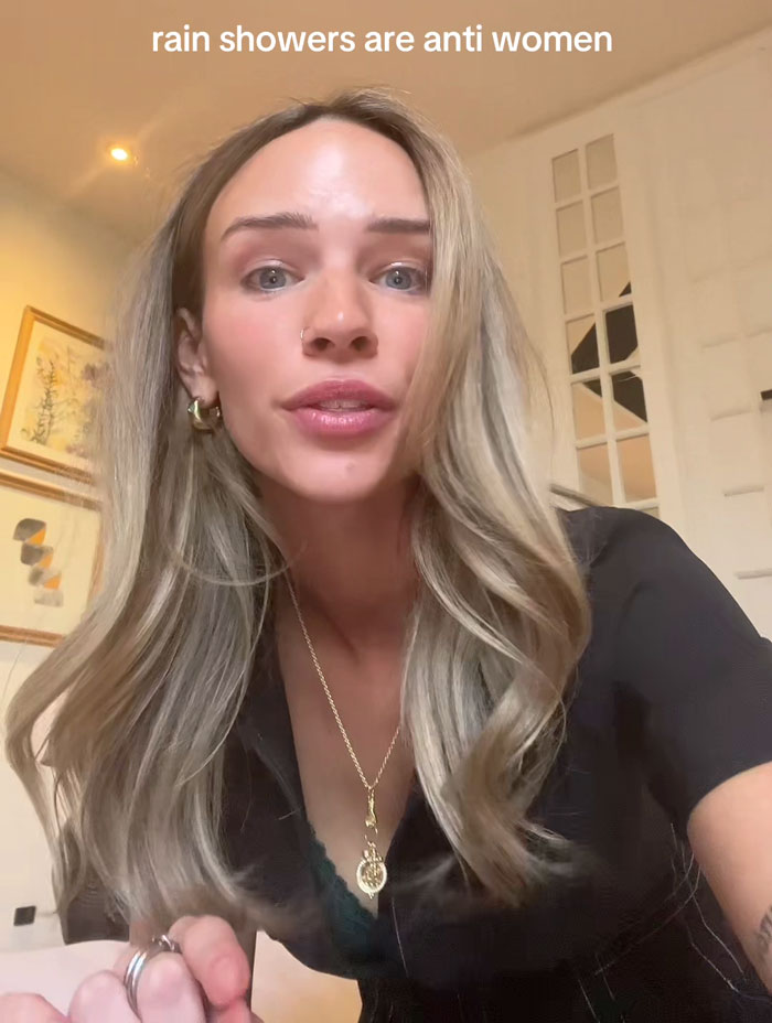 Woman expressing opinion on rain showers being anti-women, indoors, with text overlay above her head. Woman expressing opinion on rain showers being anti-women, indoors, with text overlay above her head.