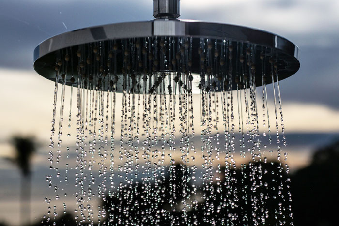 Close-up of rain showers falling from a metal showerhead against a blurred sky. Close-up of rain showers falling from a metal showerhead against a blurred sky.