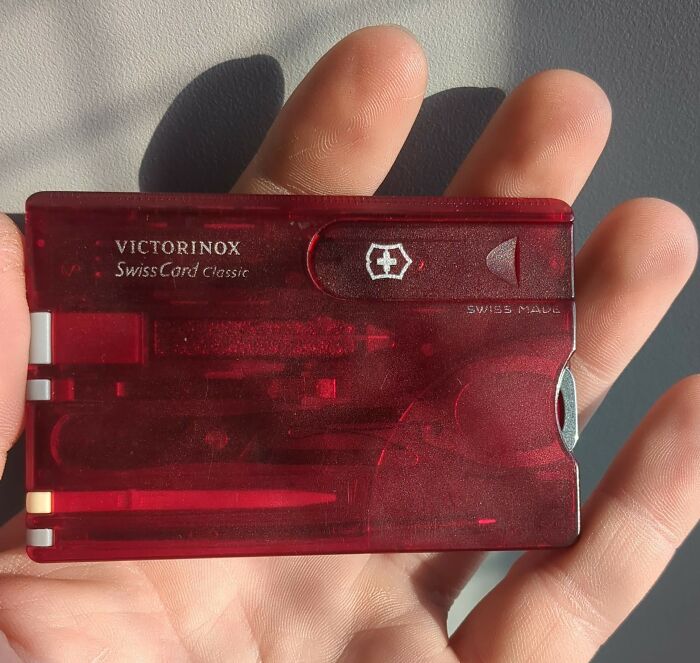 Hand holding a red SwissCard Classic, a minimalism multi-functional item with tools like a pen and scissors.