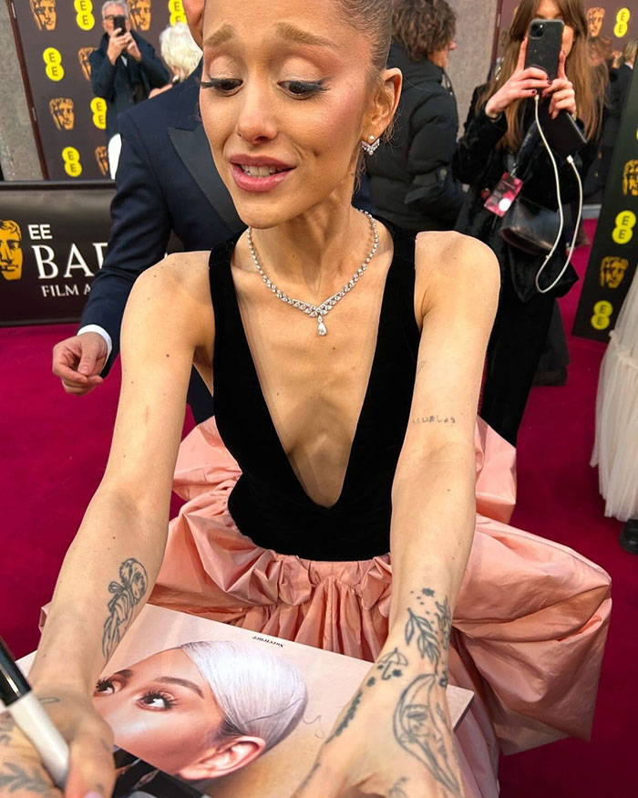 Ariana Grande signing fan's photos and albums at BAFTAs red carpet Ariana Grande signing fan's photos and albums at BAFTAs red carpet