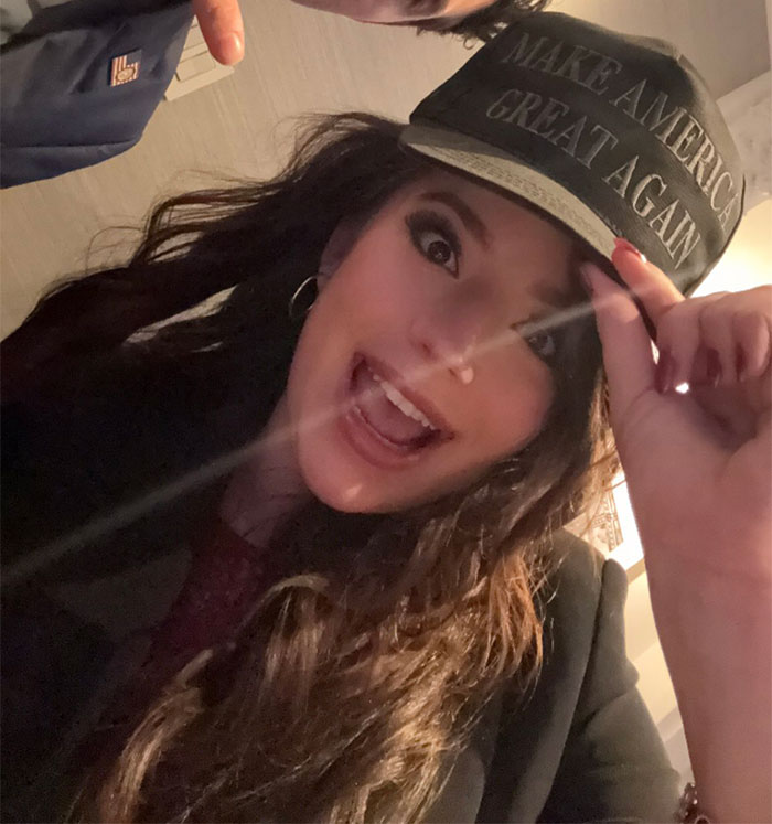 Woman with long hair wearing a "Make America Great Again" hat, smiling indoors. Woman with long hair wearing a "Make America Great Again" hat, smiling indoors.