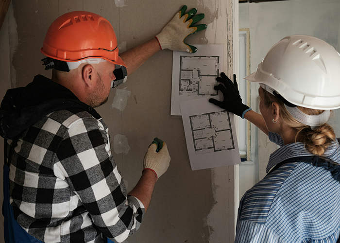 Two workers in hard hats examining floor plans for a cabin restoration. Two workers in hard hats examining floor plans for a cabin restoration.