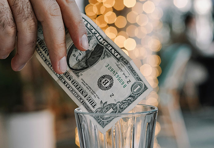 Hand placing a dollar bill in a tip jar, sparking a debate on tipping culture. Hand placing a dollar bill in a tip jar, sparking a debate on tipping culture.