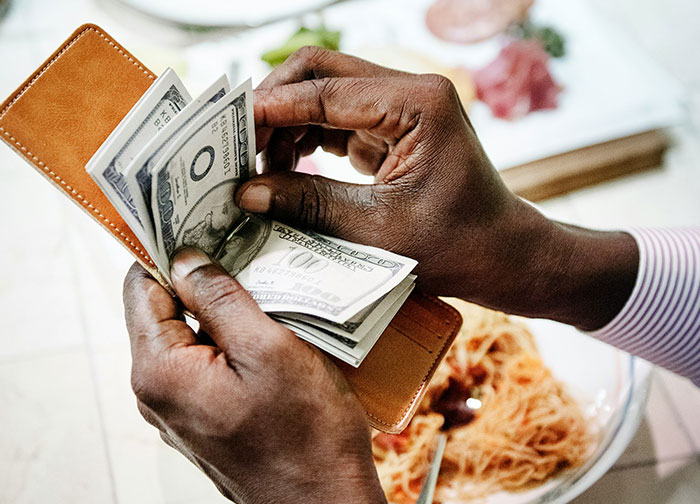 A person counting money from a wallet over a plate of pasta, sparking a debate on tipping etiquette. A person counting money from a wallet over a plate of pasta, sparking a debate on tipping etiquette.