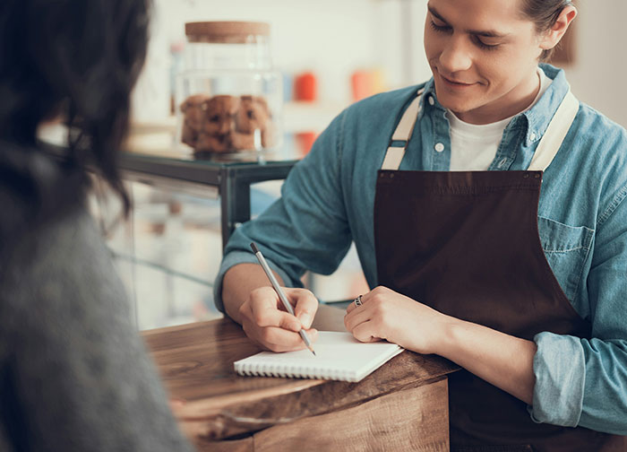 Server in a blue shirt and apron writing in a notepad, sparking debate on customer tipping practices. Server in a blue shirt and apron writing in a notepad, sparking debate on customer tipping practices.