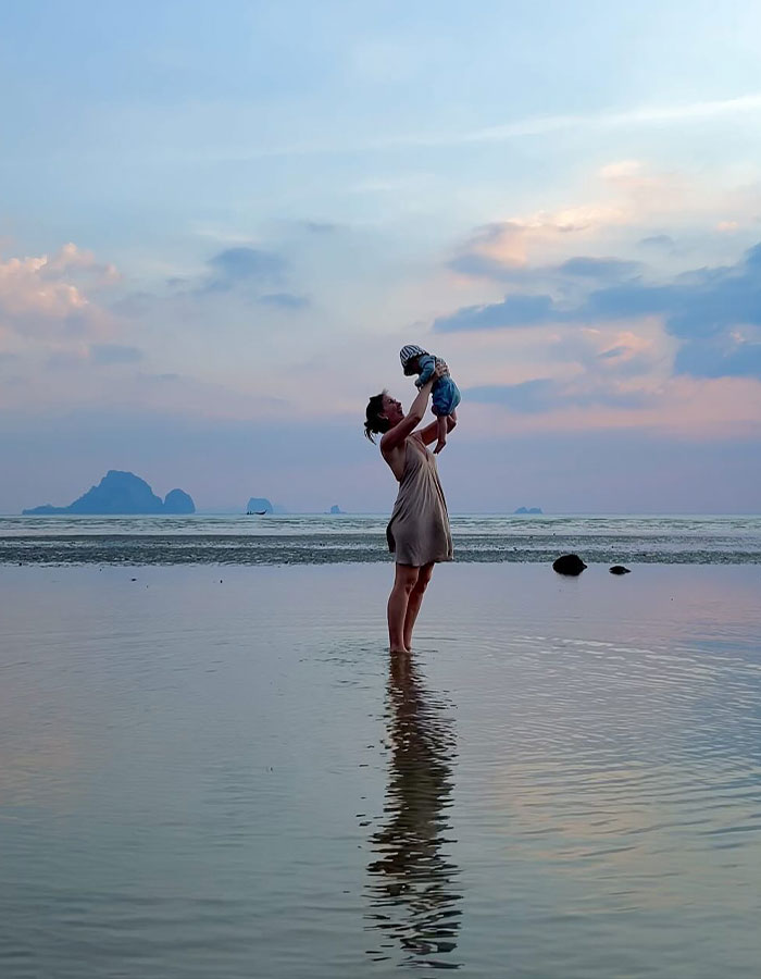 Parent holds baby at sunset on a beach in Thailand, reflecting on water. Parent holds baby at sunset on a beach in Thailand, reflecting on water.