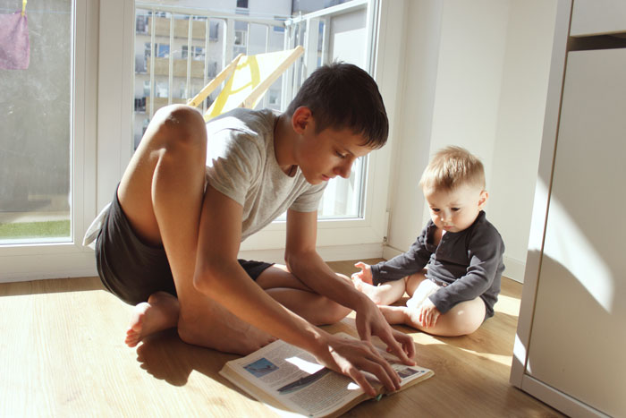 Teen babysitting in a sunlit room, reading a book to a young child, highlighting family bonding and care. Teen babysitting in a sunlit room, reading a book to a young child, highlighting family bonding and care.