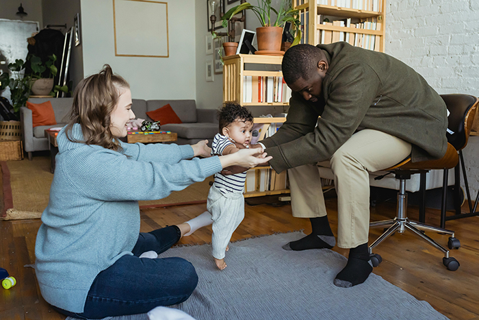 Couple playing with baby in a cozy living room, surrounded by books and plants. Couple playing with baby in a cozy living room, surrounded by books and plants.