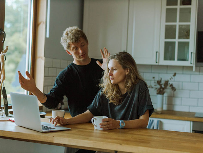 Man and woman discussing something in a kitchen setting, with a laptop and mugs on the table. Man and woman discussing something in a kitchen setting, with a laptop and mugs on the table.