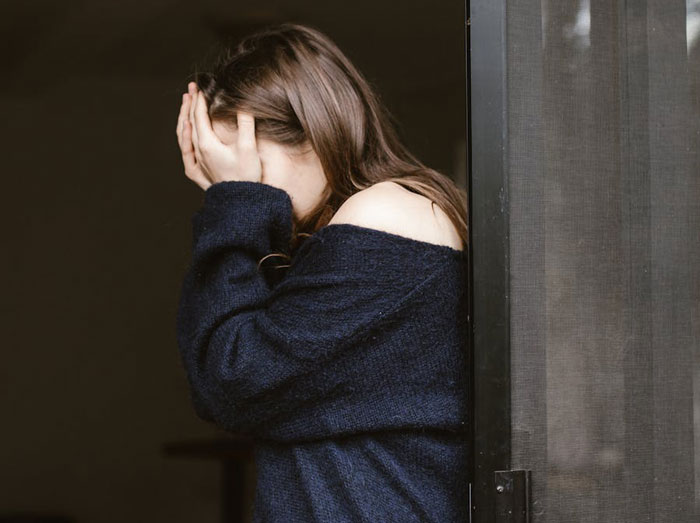 Woman covering her face, wearing a dark sweater, standing by a door. Woman covering her face, wearing a dark sweater, standing by a door.