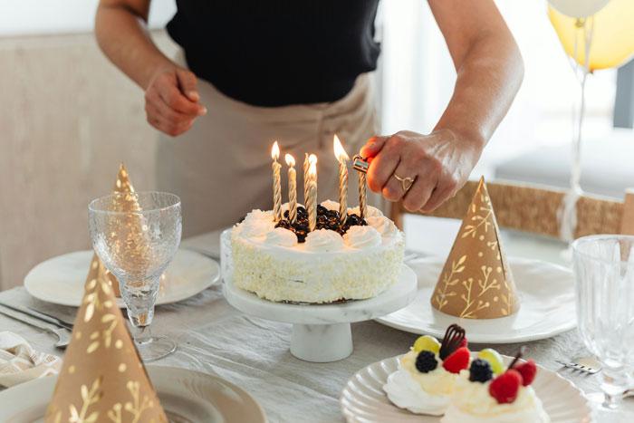 Lighting candles on a birthday cake with party hats on the table for a lady's celebration. Lighting candles on a birthday cake with party hats on the table for a lady's celebration.
