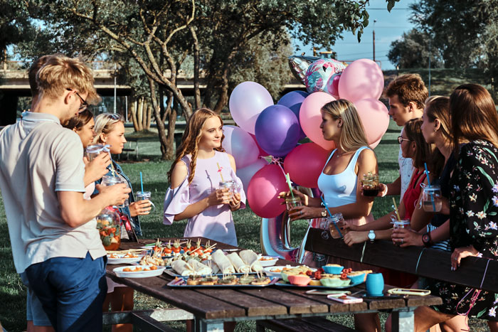 Guests celebrate lady's birthday with balloons and snacks at an outdoor picnic. Guests celebrate lady's birthday with balloons and snacks at an outdoor picnic.