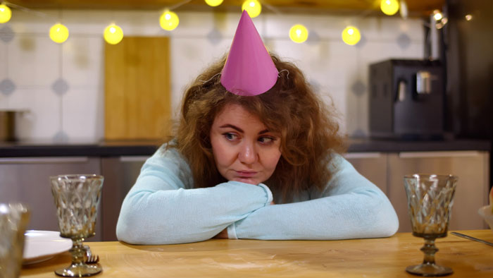 Woman in birthday hat looking pensive at a party, reflecting high celebration costs discussed online. Woman in birthday hat looking pensive at a party, reflecting high celebration costs discussed online.