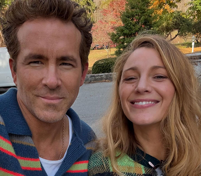 Blake Lively and Ryan Reynolds smiling outdoors in casual attire, with fall foliage in the background. Blake Lively and Ryan Reynolds smiling outdoors in casual attire, with fall foliage in the background.