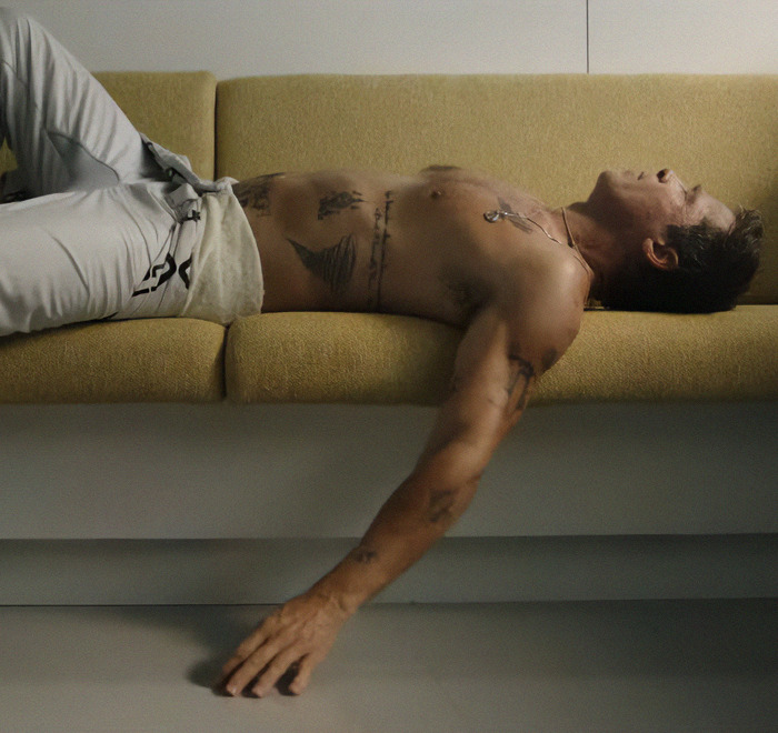 Shirtless man with tattoos relaxing on a yellow couch, showcasing body art. Shirtless man with tattoos relaxing on a yellow couch, showcasing body art.