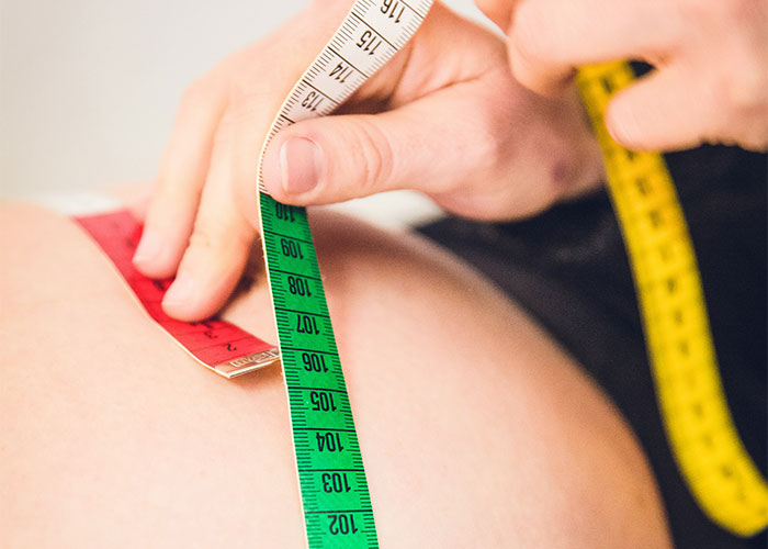 Hands using measuring tape on skin, highlighting health and weight issues. Hands using measuring tape on skin, highlighting health and weight issues.