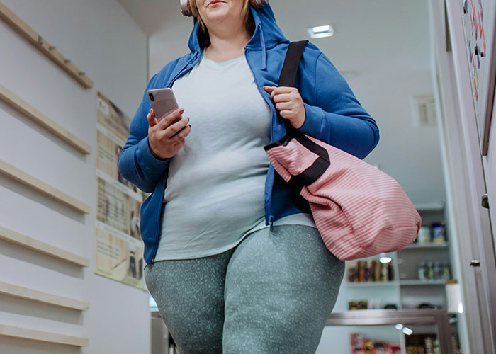 Woman in workout clothes holding a phone and bag, related to health and weight discussion. Woman in workout clothes holding a phone and bag, related to health and weight discussion.