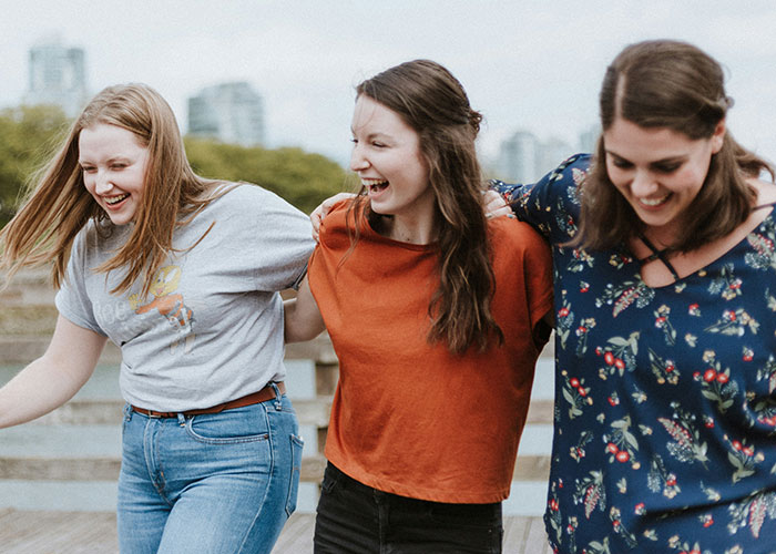 Three friends laughing and walking outdoors, highlighting friendship dynamics and health conversations. Three friends laughing and walking outdoors, highlighting friendship dynamics and health conversations.