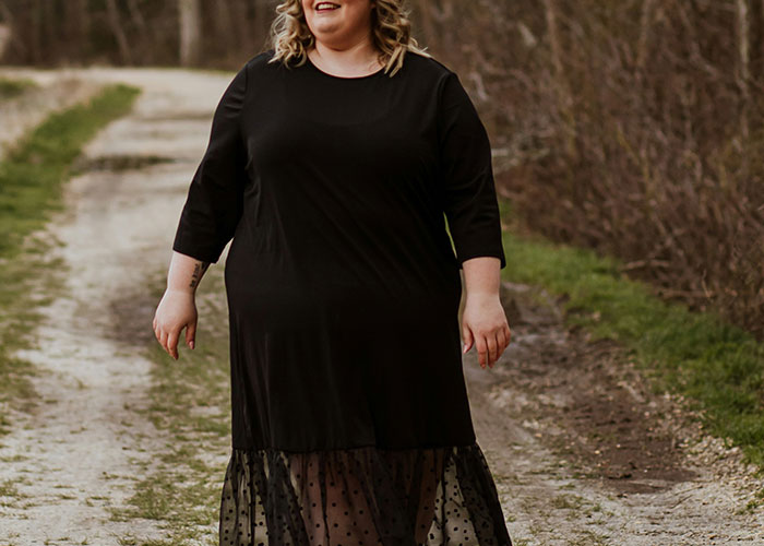 Person in a black dress walking on a dirt path, related to conflict over health and weight during a girls' night. Person in a black dress walking on a dirt path, related to conflict over health and weight during a girls' night.