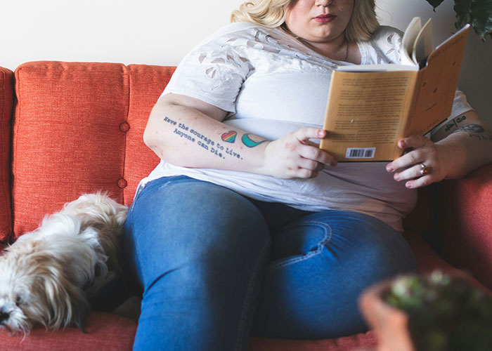 Woman reading on a couch with a dog, related to conflict over health and weight. Woman reading on a couch with a dog, related to conflict over health and weight.