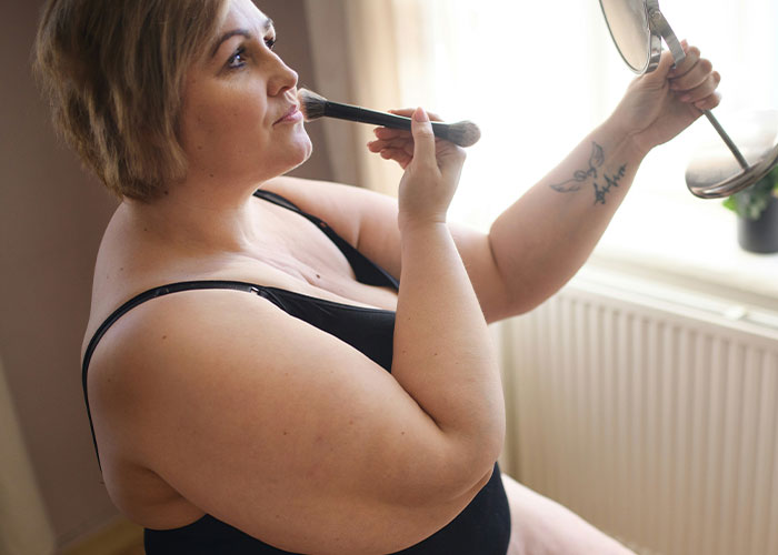 Woman applying makeup, holding a mirror, during a girls' night focused on health and weight discussions. Woman applying makeup, holding a mirror, during a girls' night focused on health and weight discussions.