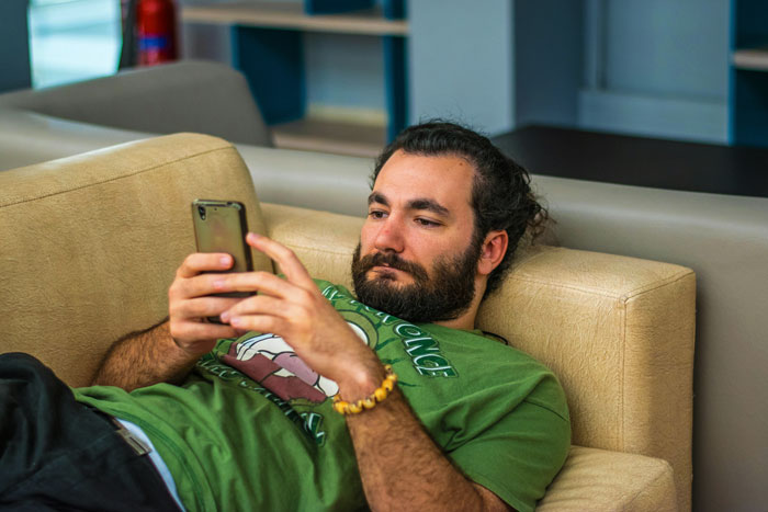 Man lying on a couch, looking at his phone after canceling a planned date. Man lying on a couch, looking at his phone after canceling a planned date.