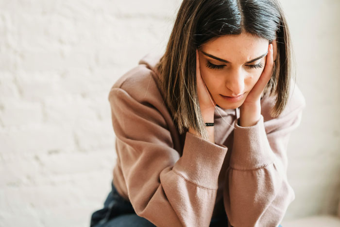 Woman looks upset after boyfriend cancels date, sitting in a beige sweater, head in hands. Woman looks upset after boyfriend cancels date, sitting in a beige sweater, head in hands.
