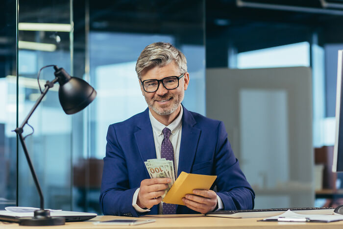 Man in a business suit counting money at his desk, highlighting professions with higher rates of infidelity. Man in a business suit counting money at his desk, highlighting professions with higher rates of infidelity.