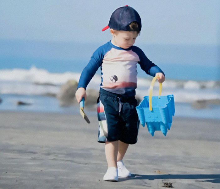 A young boy on the beach with a blue bucket and spade, wearing a cap. A young boy on the beach with a blue bucket and spade, wearing a cap.