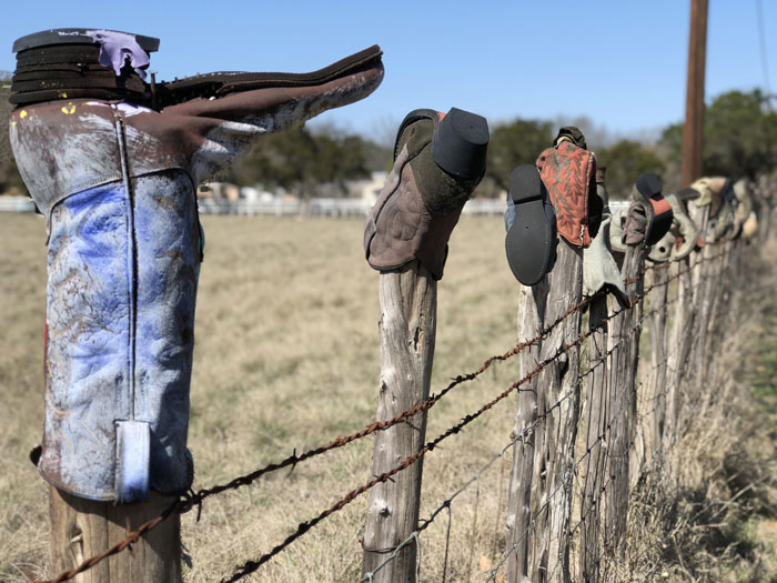 Cowboy boots stuck on wooden fence posts in a rural field setting. Cowboy boots stuck on wooden fence posts in a rural field setting.