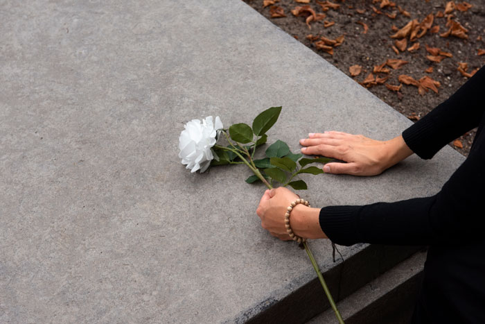 Person placing a white rose on a gravestone, symbolizing loss and remembrance of a coworker. Person placing a white rose on a gravestone, symbolizing loss and remembrance of a coworker.