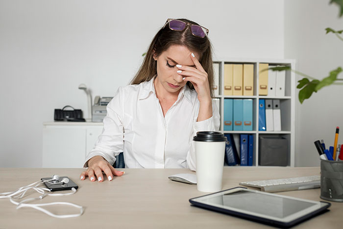 Woman in an office looking stressed, sitting at a desk with a coffee cup and gadgets. Woman in an office looking stressed, sitting at a desk with a coffee cup and gadgets.