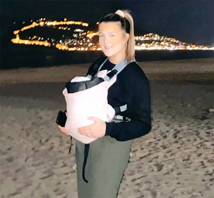 Teen with baby carrier on beach at night, city lights in background, related to medical case from 1988. Teen with baby carrier on beach at night, city lights in background, related to medical case from 1988.