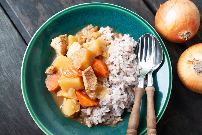 A plate of chicken stew and rice, positioned beside onions and cutlery, illustrating a multi-functional meal concept.