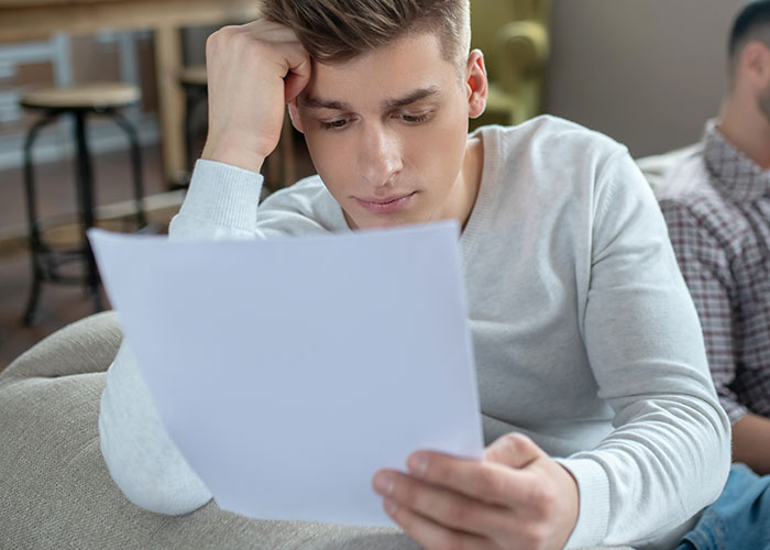 Teen reading letter on couch, deep in thought, reflecting on brother's final words. Teen reading letter on couch, deep in thought, reflecting on brother's final words.