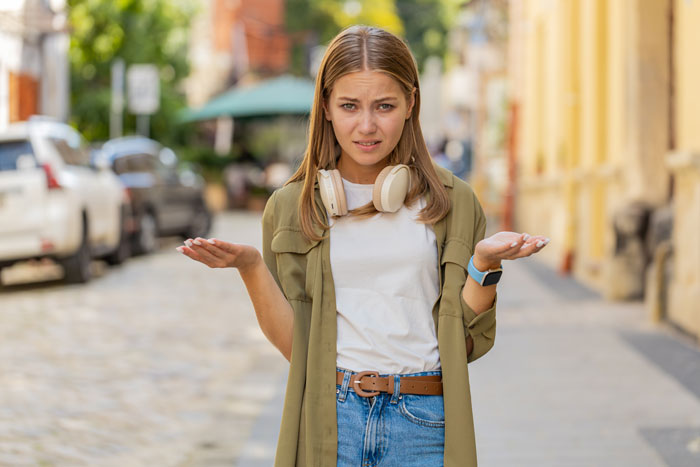Young woman looking confused on a city street, wearing headphones, pondering dating advice for her dad's younger girlfriend. Young woman looking confused on a city street, wearing headphones, pondering dating advice for her dad's younger girlfriend.