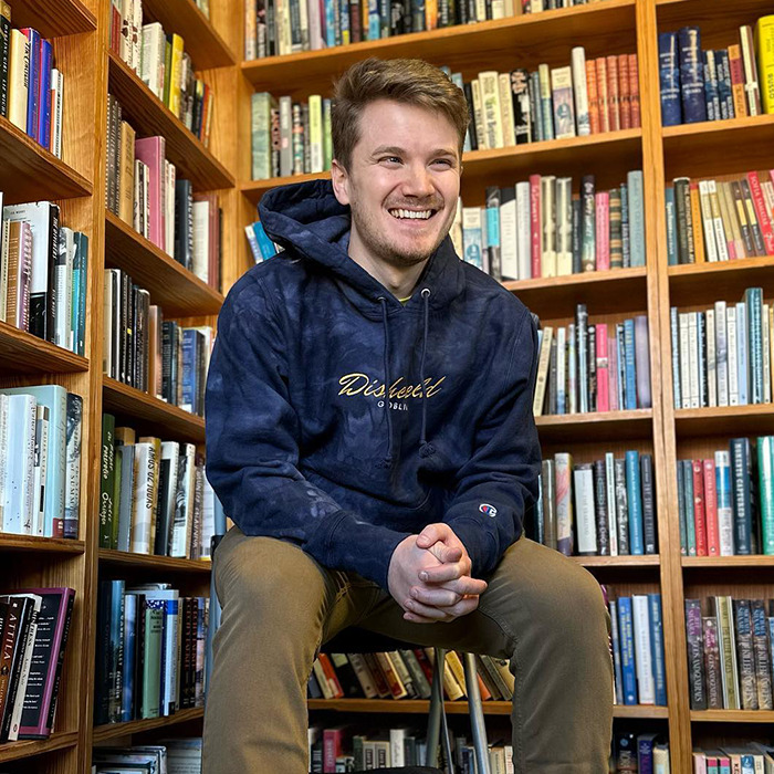 Person in a cozy library, wearing a dark hoodie, surrounded by shelves filled with bookshelves, related to BookTube crisis. Person in a cozy library, wearing a dark hoodie, surrounded by shelves filled with bookshelves, related to BookTube crisis.