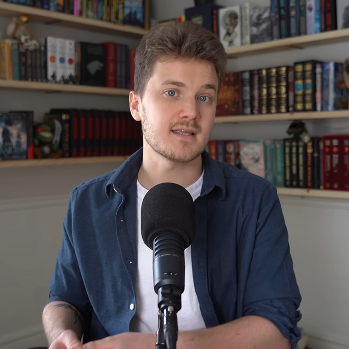 Person discussing BookTube crisis in a library setting with a microphone. Person discussing BookTube crisis in a library setting with a microphone.
