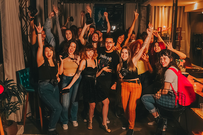 A joyful group of people celebrating indoors, some holding cameras, with raised arms, highlighting a vibrant social gathering. A joyful group of people celebrating indoors, some holding cameras, with raised arms, highlighting a vibrant social gathering.