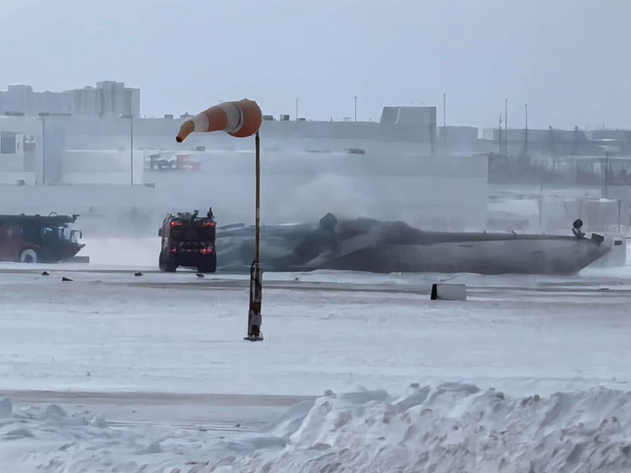 Delta Airlines plane upside down after crash landing, surrounded by snow and emergency vehicles. Delta Airlines plane upside down after crash landing, surrounded by snow and emergency vehicles.