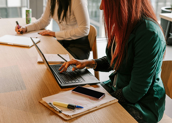 Two women at a table, one using a laptop; highlights probation and punctuality in a work setting. Two women at a table, one using a laptop; highlights probation and punctuality in a work setting.