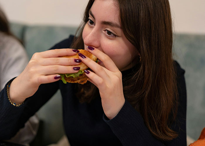 Woman with long hair eating a burger, illustrating being late to a job. Woman with long hair eating a burger, illustrating being late to a job.