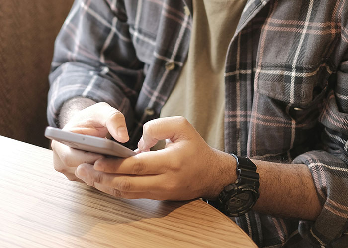 Man checking phone, wearing a plaid shirt, related to getting girlfriend a job. Man checking phone, wearing a plaid shirt, related to getting girlfriend a job.