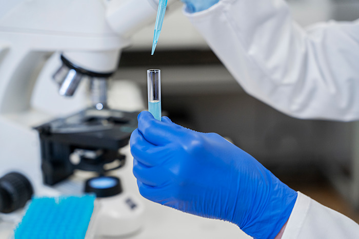 Lab technician using DNA testing equipment, holding a pipette and test tube. Lab technician using DNA testing equipment, holding a pipette and test tube.