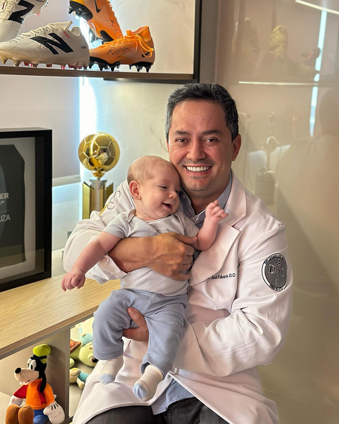 Doctor in a white coat smiling while holding a happy baby, with sports memorabilia in the background. Doctor in a white coat smiling while holding a happy baby, with sports memorabilia in the background.