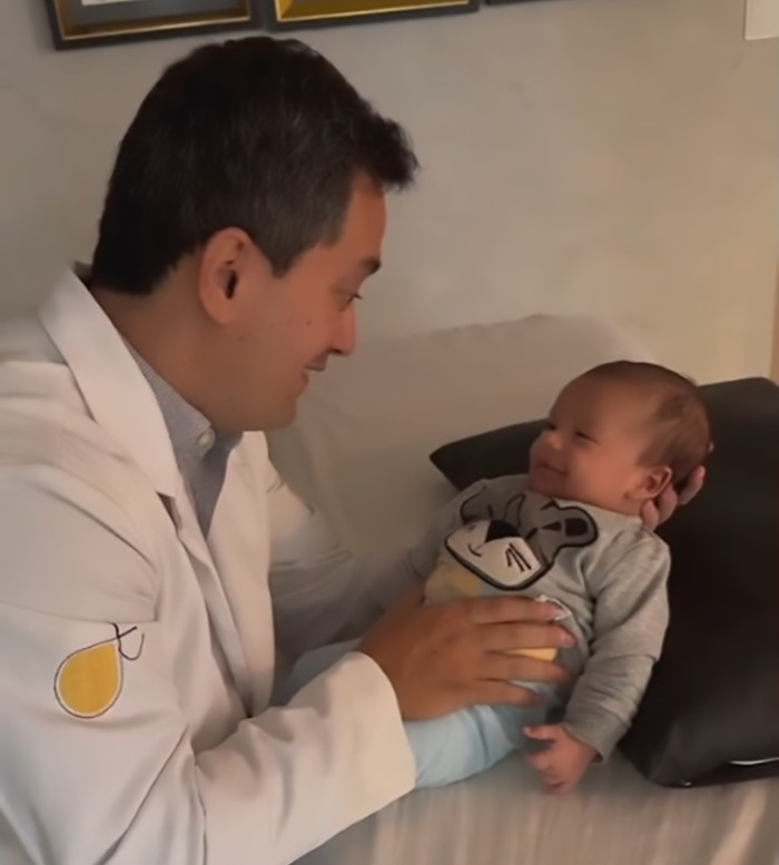 Doctor in white coat using baby farting tips on a smiling infant lying on a pillow. Doctor in white coat using baby farting tips on a smiling infant lying on a pillow.