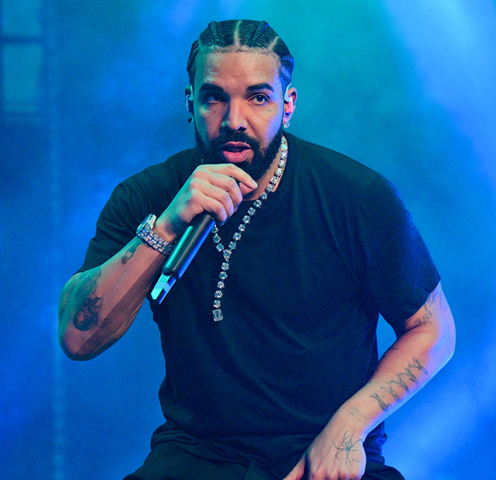 Man performing on stage with a microphone, wearing a black shirt and chain, in blue lighting. Man performing on stage with a microphone, wearing a black shirt and chain, in blue lighting.