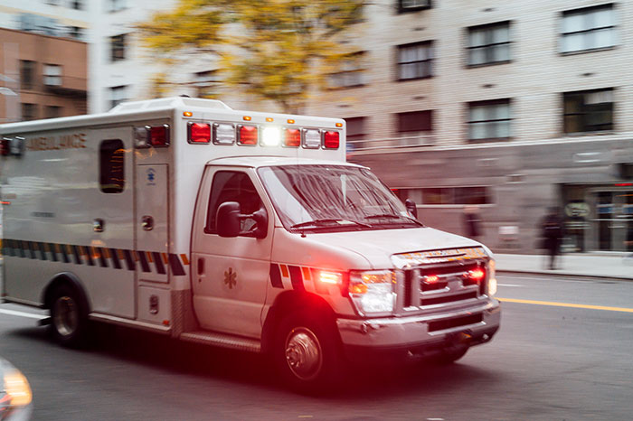 An ambulance driving with lights on in an urban setting. An ambulance driving with lights on in an urban setting.