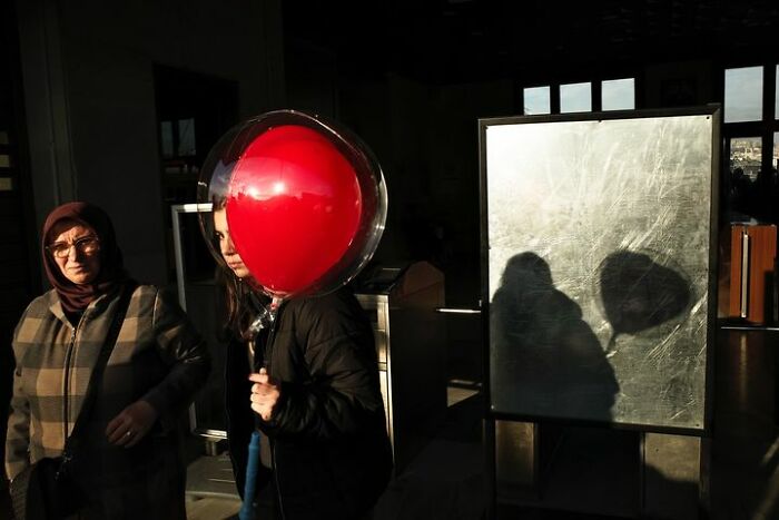 Two people walking; one holding a red balloon, casting a shadow that shows Gökhan Arer's unique street view.