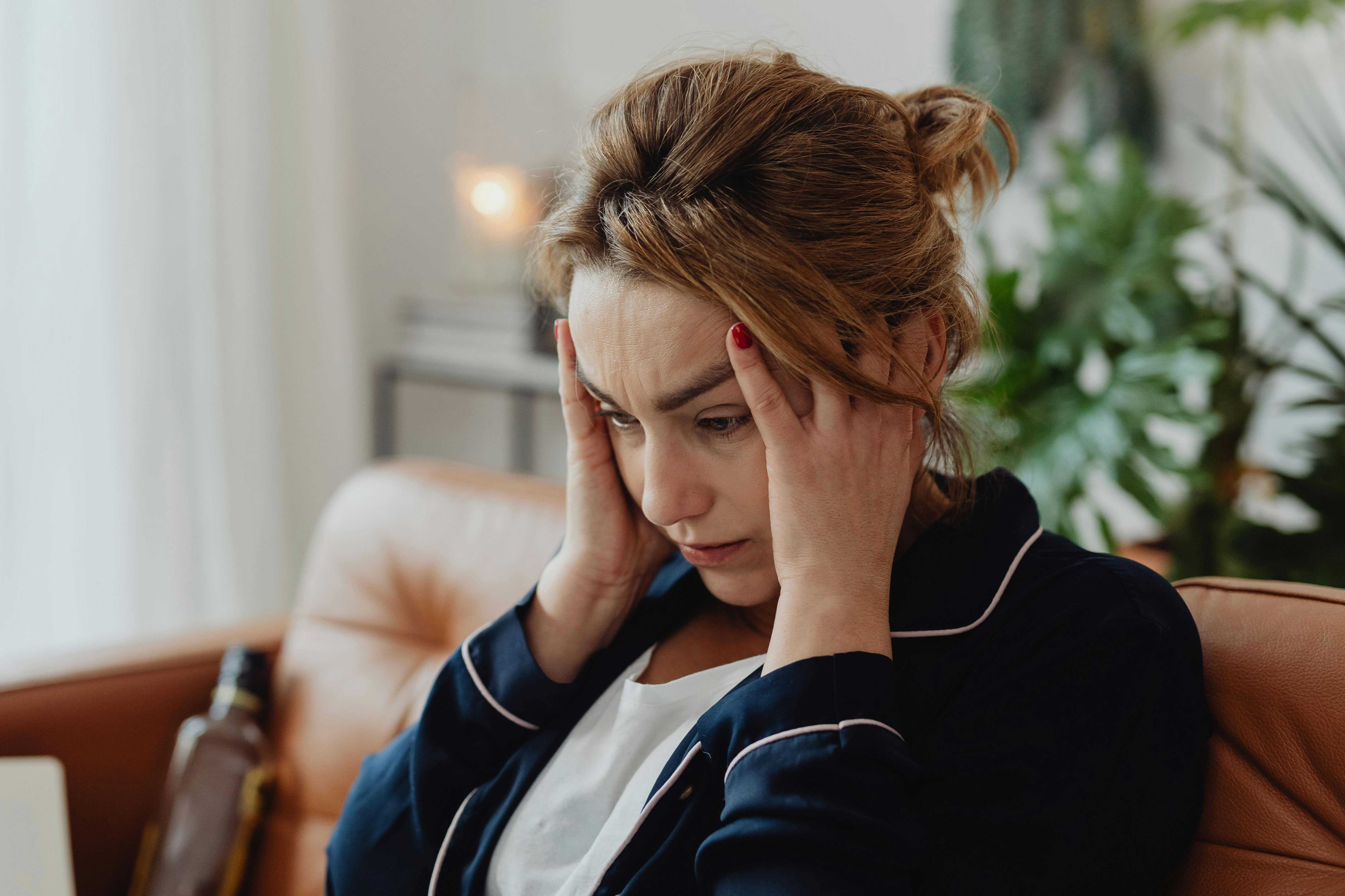 A worried mom sits on a couch with hands on temples, pondering her son's cat allergy. A worried mom sits on a couch with hands on temples, pondering her son's cat allergy.